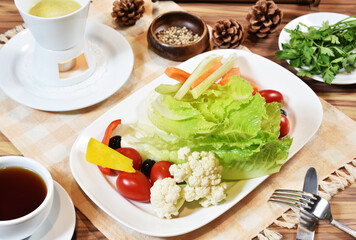 Warm salad with  lettuce, cherry tomatoes, slices of yellow bell pepper, olives, sticks of celery and carrot sticks. 