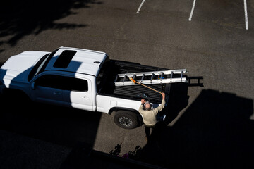 View from rooftop of a senior caucasian man removing a broom from the bed of a white pickup truck, property maintenance  © knelson20