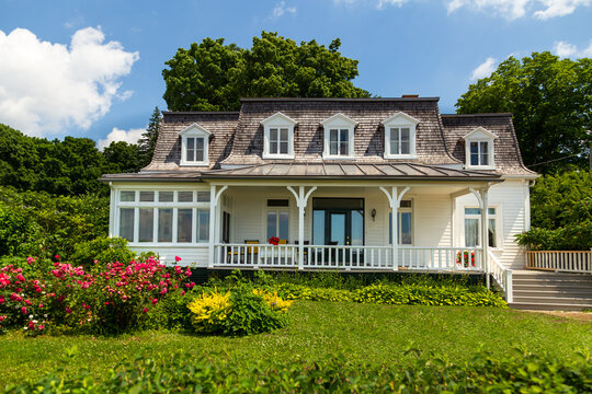 Asymmetrical Second Empire style white country cottage with steeply-pitched mansard roof, seen during a sunny summer day in the Island of Orleans, Quebec, Canada