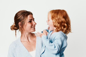 Happy mother and daughter in matching sweaters smiling at each other on white background