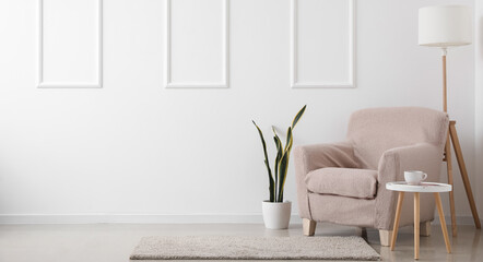 Interior of light living room with beige armchair, table and lamp