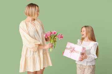 Beautiful young woman holding bouquet of tulips and her cute little daughter with gift box on green background