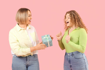 Beautiful happy women in stylish jeans with gift box on pink background