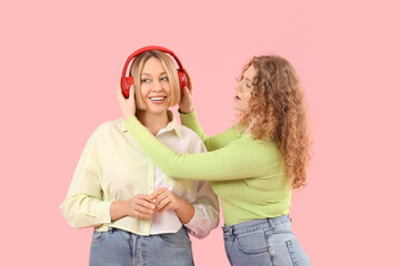 Beautiful happy women in stylish jeans with headphones on pink background