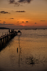 Golden hues of sunset paint the sky and reflect on the tranquil waters, creating a serene and picturesque scene by the pier