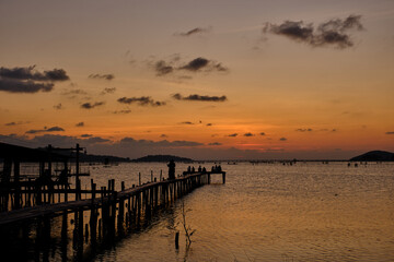 Golden hues of sunset paint the sky and reflect on the tranquil waters, creating a serene and picturesque scene by the pier