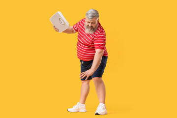 Overweight mature man with scales on yellow background. Weight loss concept