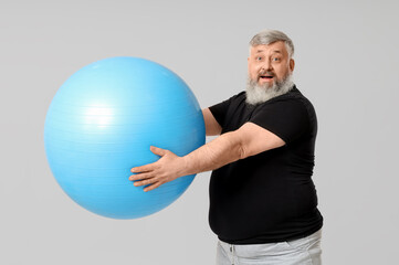 Overweight shocked mature man with fitness ball on grey background. Weight loss concept