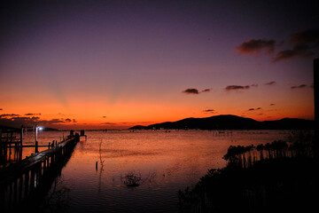 Golden hues of sunset paint the sky and reflect on the tranquil waters, creating a serene and picturesque scene by the pier