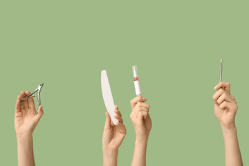 Female hands with cuticle oil pen, nail file and cutter on green background