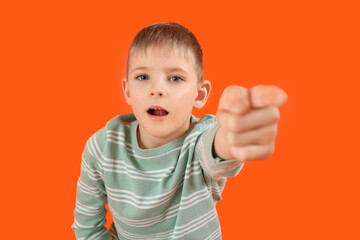 Shocked little boy pointing at viewer on orange background