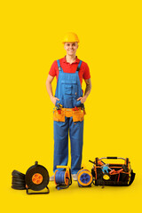 Obraz premium Young male electrician with tool bag and extension cable reels on yellow background