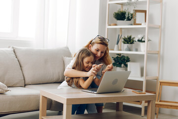 Mother and daughter bonding moment, exploring educational content on a laptop while sitting comfortably on a cozy couch