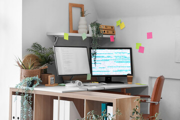 Interior of light office with programmer's desk, plants and sticky notes