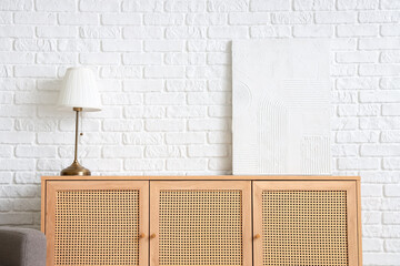 Lamp and picture on wooden cabinet near white brick wall in room