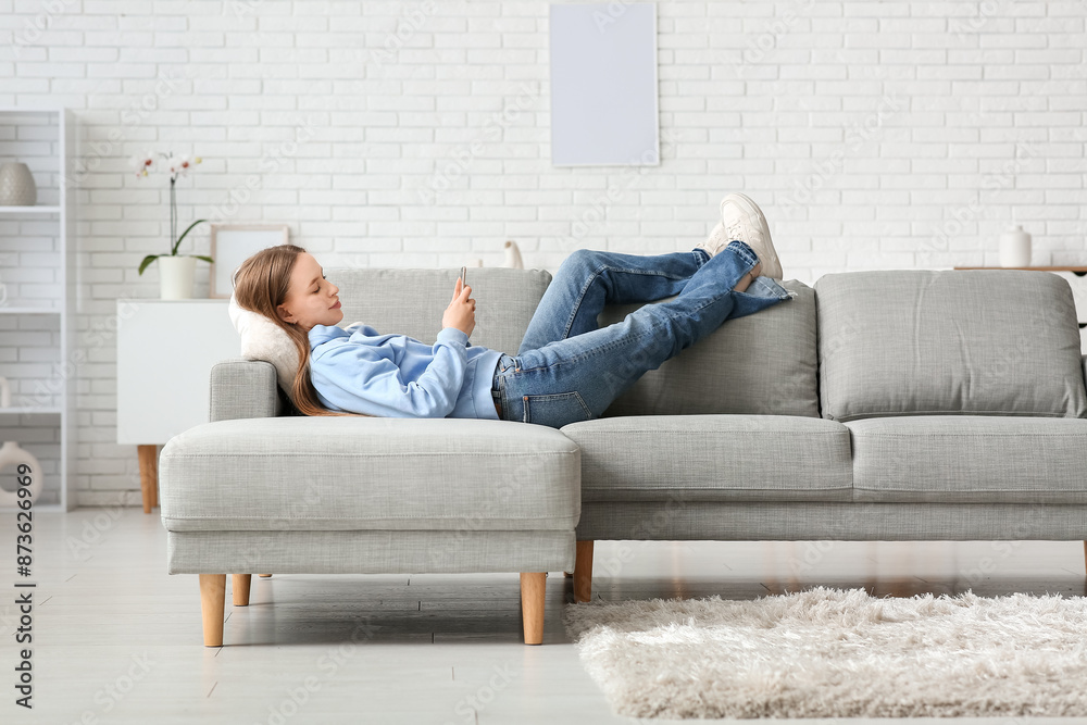 Sticker Young pretty woman lying and chatting with mobile phone on sofa in stylish living room