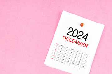 December 2024 calendar page and wooden push pin on pink background.