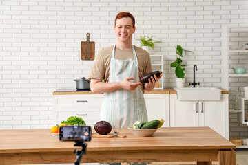 Young man with fresh vegetables recording cooking video in kitchen