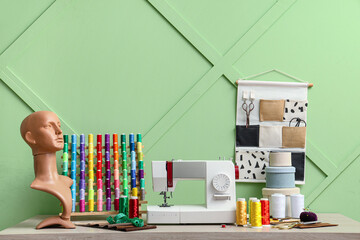 Tailor's workplace with sewing machine, mannequin head and set of colorful threads near green wall
