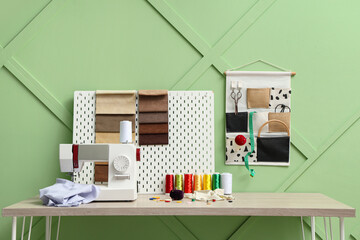 Tailor's workplace with sewing machine and threads near green wall