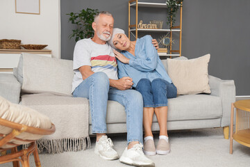 Mature woman after chemotherapy with her husband sitting on sofa at home