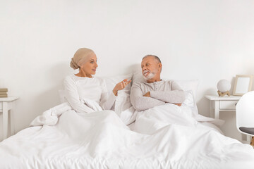 Mature woman after chemotherapy with her husband lying in bedroom