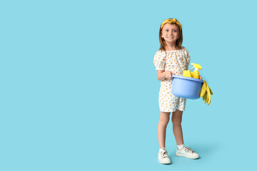 Cute little happy girl with basin of different cleaning supplies on blue background