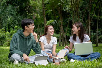 A group of cheerful Asian students in casual clothes sits and talks in the green park, enjoying their conversation while working on their co-project together.