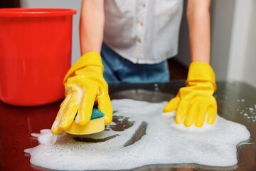 Woman in rubber gloves cleaning table with sponge and bucket of soapy water in front of red bucket