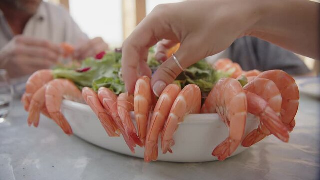 Family sitting at dining table takes turns to take king prawn arranged in bowl