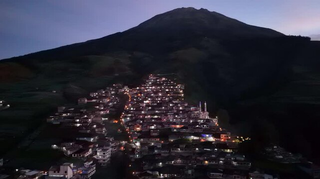 Aerial night shot of village on the slope of mountain with light on with slightly foggy weather. Nepal Van Java Village, Indonesia. 4K drone shot.
