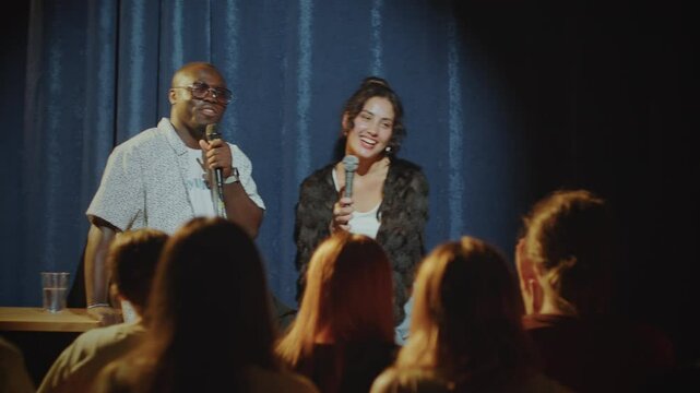 Young cheerful African American man and Caucasian woman performing comedy together on stage in front of audience in stand-up club
