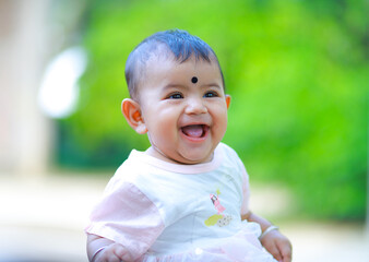 Smiling portrait of a south asian baby girl, six months old girl smiling with joy sitting outdoor