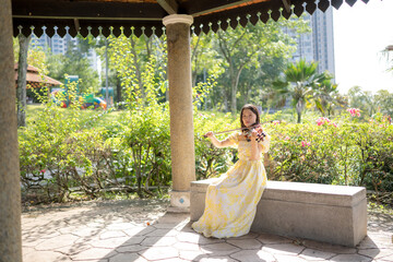 Young Chinese Malaysian woman in her 20s playing violin inside a Western-style gazebo in a large park in Bukit Jalik, Malaysia, wearing a yellow dress.  © Masakazu Tokashiki