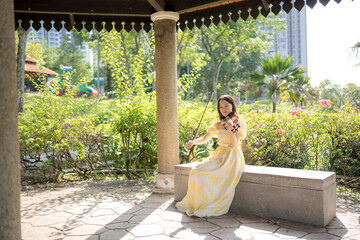 Young Chinese Malaysian woman in her 20s playing violin inside a Western-style gazebo in a large park in Bukit Jalik, Malaysia, wearing a yellow dress.  © Masakazu Tokashiki