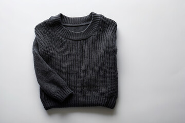 Cozy black sweater lies flat on a light gray background, empty space around it, perfect for adding text or graphics, showcasing winter fashion apparel.