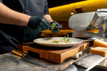 close up in restaurant in a rib bar in the central hall with yellow lighting, a chef in black gloves puts a pillow of fresh herbs on a plate