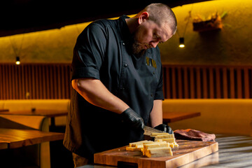in a restaurant in a rib bar in the central hall, a chef in black gloves on a wooden board cuts cheese into strips for making cheese sticks