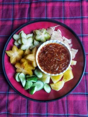 A bowl of healthy fresh fruit salad on a wooden background complete with peanut sauce.Top view