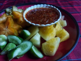 A bowl of healthy fresh fruit salad on a wooden background complete with peanut sauce.Top view