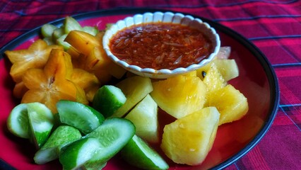 A bowl of healthy fresh fruit salad on a wooden background complete with peanut sauce.Top view