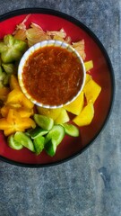 A bowl of healthy fresh fruit salad on a wooden background complete with peanut sauce.Top view