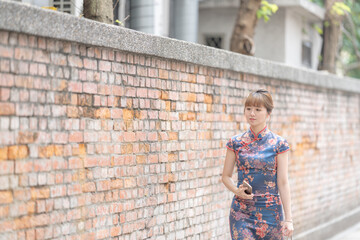 Young Taiwanese woman in her 20s wearing a blue cheongsam and carrying a red bag, strolling through the streets of Wanhua District, Taipei, Taiwan