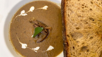 Mushroom Soup in craft bowl on wooden table. Mushroom champignon soup with bread and fresh mushrooms. ZUPPA DI FUNGHI (Mushroom soup served with sourdough). top view.