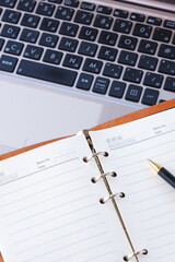 リング式のシステム手帳を開いて、ノートパソコンでデスクワークをしているイメージ
