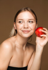 Woman Holding Apple Against Brown Background. A young Caucasian woman with clear, glowing skin holding an apple against a brown background, symbolizing health and beauty.