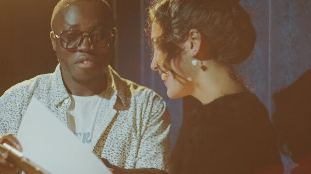 African American stand-up show host discussing performance script with young female comedian standing on stage under spotlight