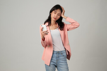 pensive asian woman wearing formal casual outfit holding her mobile phone with thinking gesture on isolated background