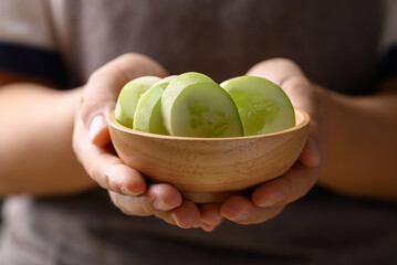 Sliced cucumber in wooden bowl holding by hand, Organic vegetable, Food ingredient