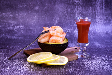 Shrimp in half an avacado on a wooden board with lemon slices and cocktail on a gray background